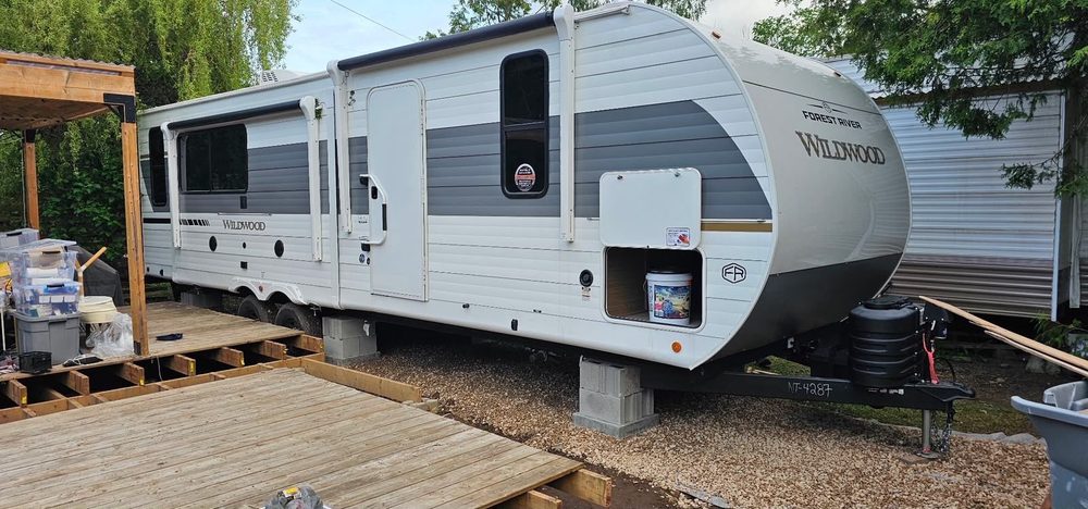 White travel trailer sitting level on blocking beside a newly built wooden deck